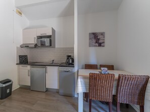 A compact kitchen with a dishwasher, microwave, and coffee maker. There is a dining table with wicker chairs and a painting on the wall. - 4-guest Stay Near Moutchic Beach (Lacanau)