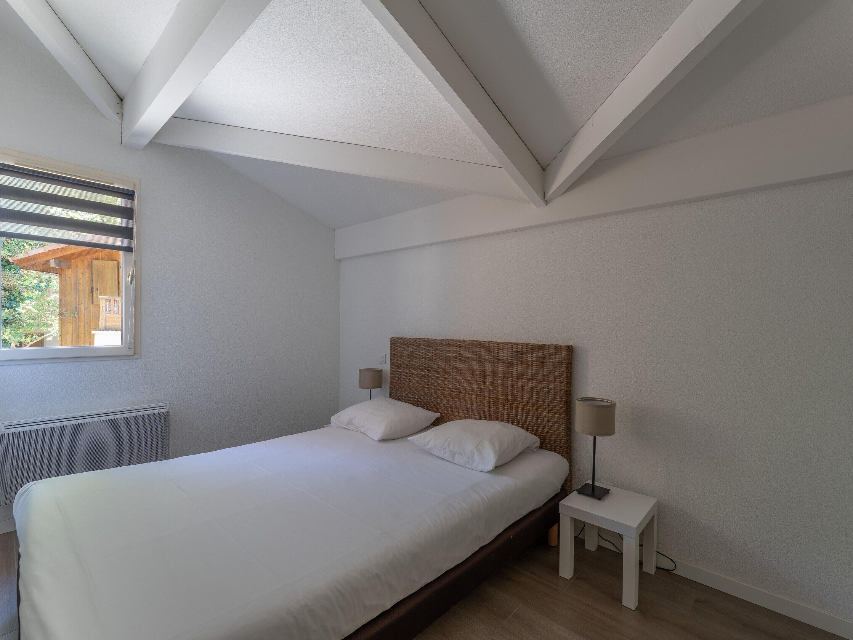 Un dormitorio con cama, mesita de noche, lámpara, ventana y radiador.