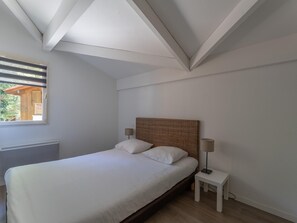 A bedroom with a bed, a nightstand, a lamp, a window, and a radiator. - 4-guest Stay Near Moutchic Beach (Lacanau)