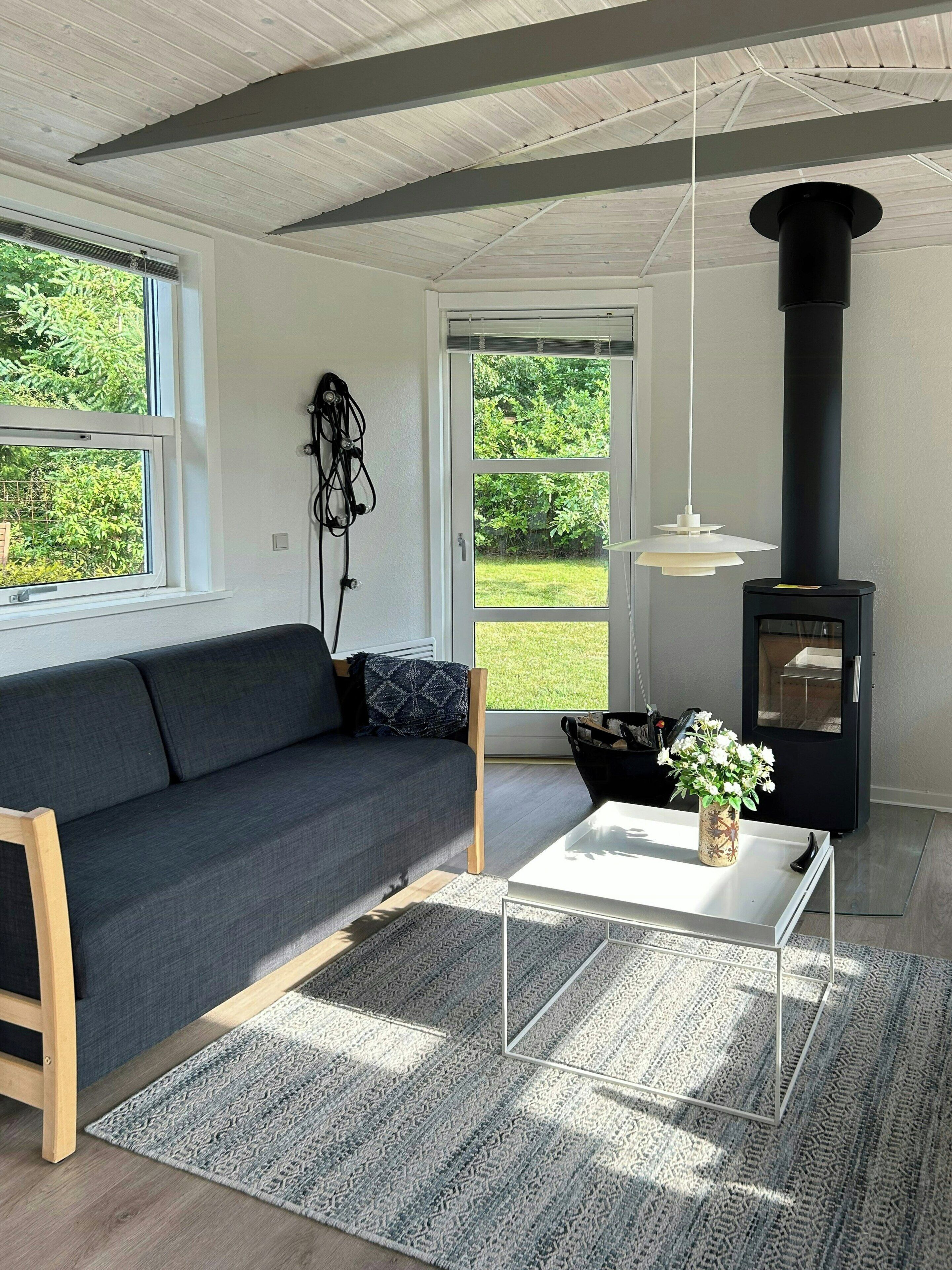 Un salon moderne avec un canapé, une table basse, une cheminée noire et une vue sur l’extérieur.
