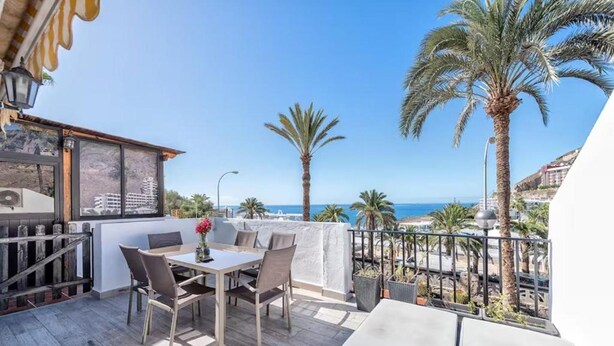 A terrace with a table and chairs, a sofa, and a view of the sea. - Palm Beach Suite - Playa del Cura (Mogán)