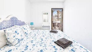 A bedroom with a bed, a nightstand, a mirror, and a view of a building through an open door. - Palm Beach Suite - Playa del Cura (Mogán)