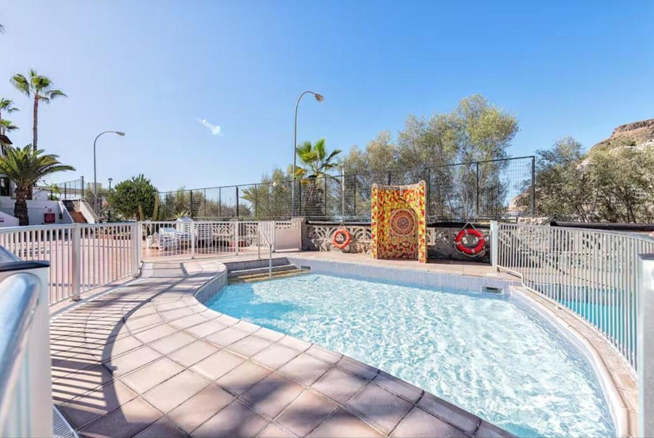 A swimming pool with a tiled deck, a lifebuoy, and a decorative wall.