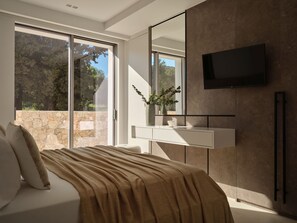 Un dormitorio moderno con una cama grande, un televisor montado en la pared y una pared de piedra visible desde la ventana.