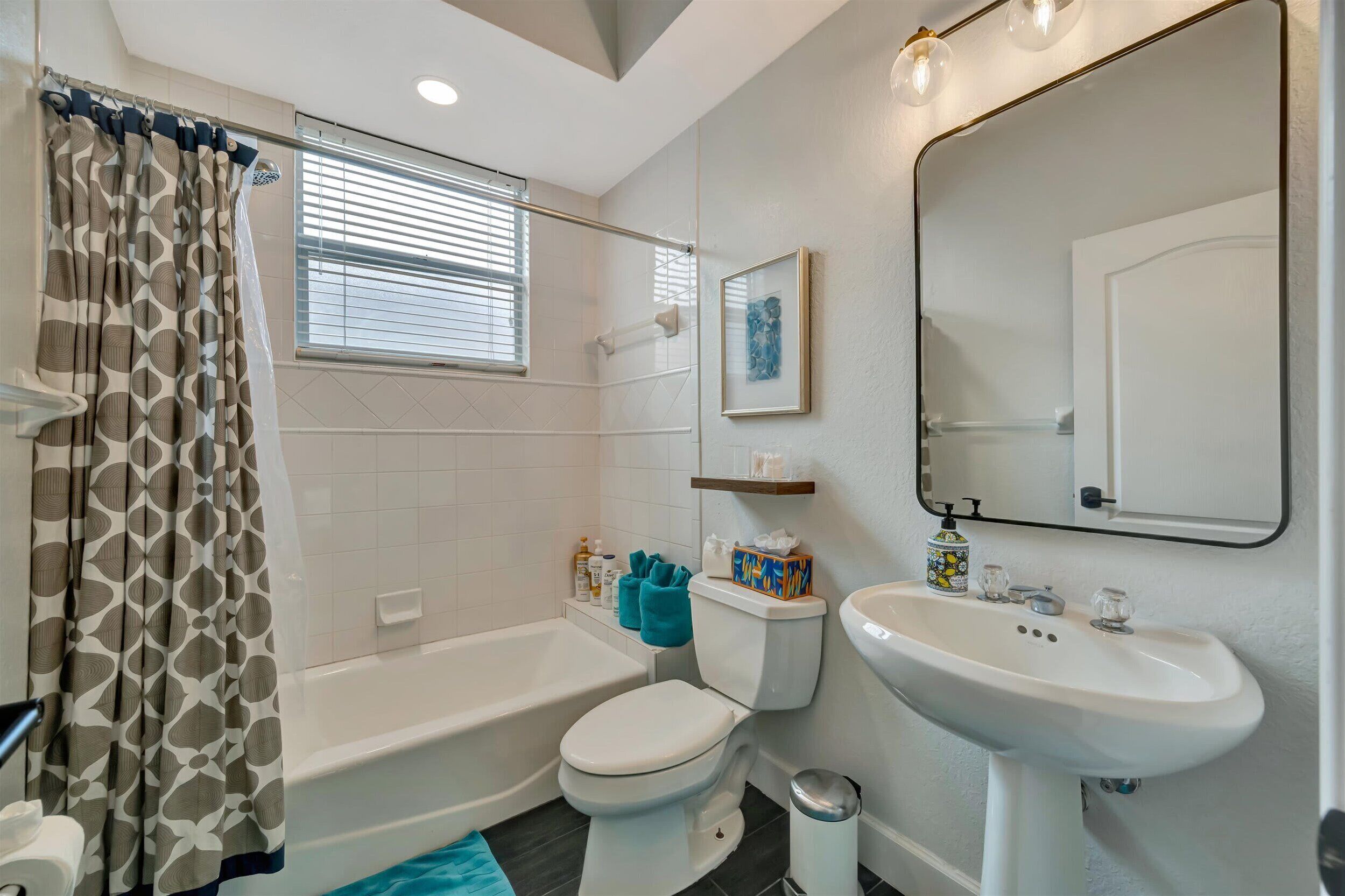 A bathroom with a bathtub, toilet, and sink, with a shower curtain and a framed picture on the wall.