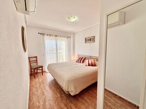 A bedroom with a bed, a chair, a window with curtains, a wall-mounted picture, and a ceiling light. - Spacious 2-bedroom apartment with canal views (La Manga del Mar Menor)