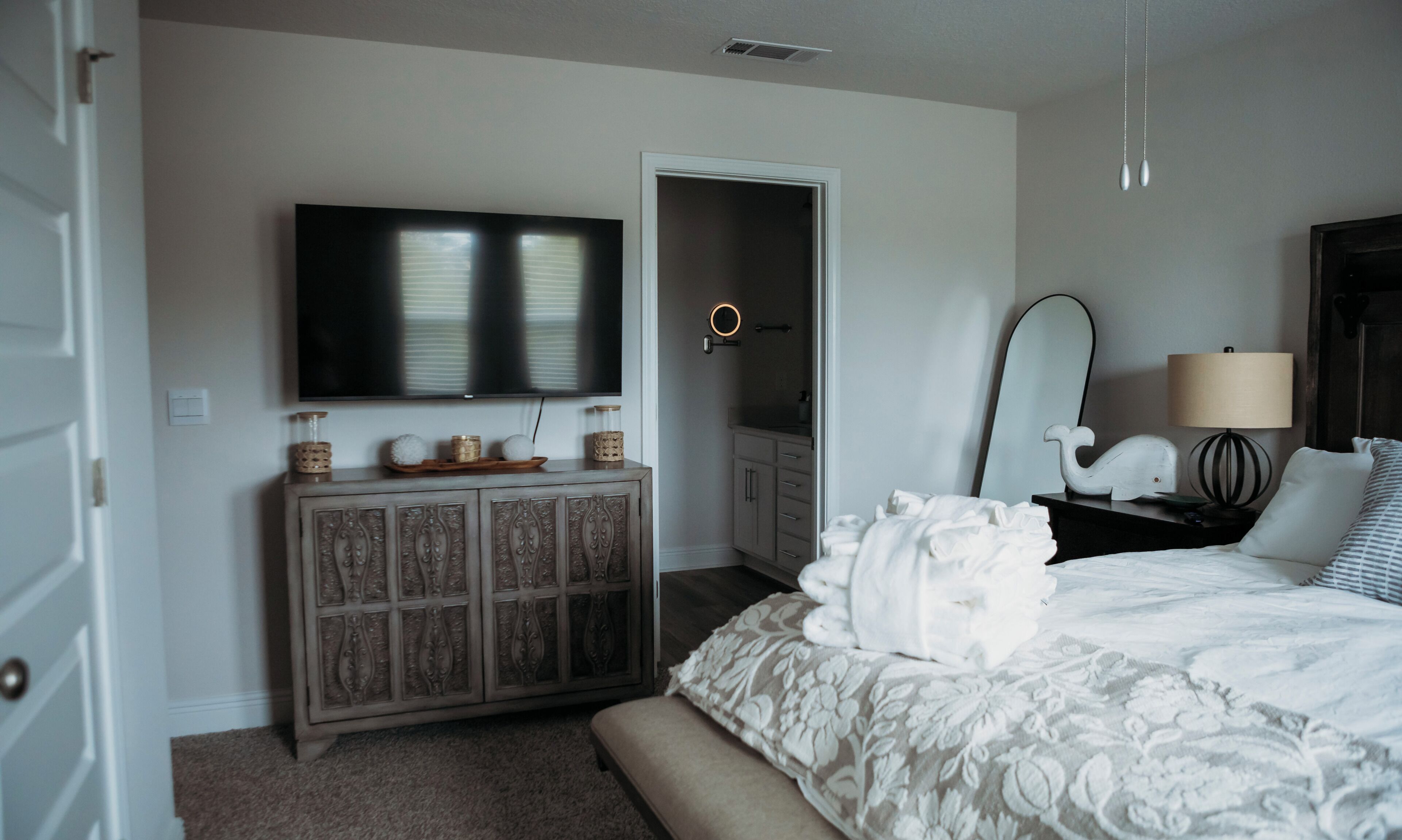 Une chambre à coucher comprenant un lit, une commode, un téléviseur, un miroir et une table de chevet avec une lampe.