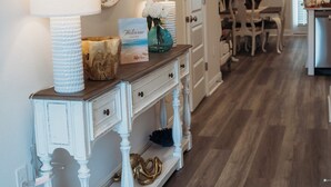 A hallway with a white console table, a mirror, a welcome sign, and a dining area in the background. - Welcome to Easy Breezy.  Luxury Coastal Getaway, Minutes From Two Beaches. (Gulf Breeze)