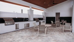 An outdoor kitchen with a grill, a built-in oven, and a seating area with chairs and a table. - Welcome to Easy Breezy.  Luxury Coastal Getaway, Minutes From Two Beaches. (Gulf Breeze)