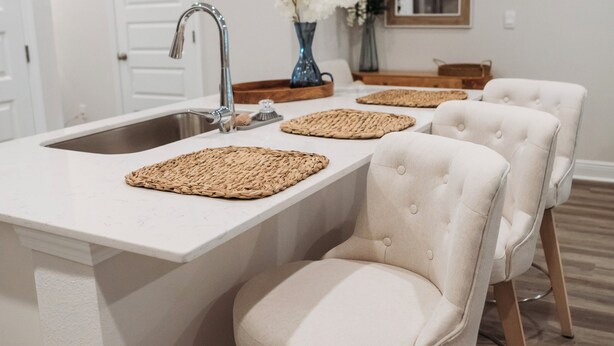 A modern kitchen with a white countertop, stainless steel sink, and two upholstered bar stools. - Welcome to Easy Breezy.  Luxury Coastal Getaway, Minutes From Two Beaches. (Gulf Breeze)