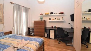 Ein Schlafzimmer mit Bett, Schreibtisch, Stuhl und Regalen mit verschiedenen Gegenständen.