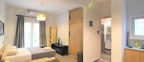 A modern hotel room with a bed, bedside table, lamp, and a view of the hallway.