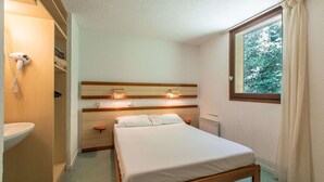 Un dormitorio con cama, mesitas de noche, una lámpara en una repisa empotrada y ventana con vistas a árboles.