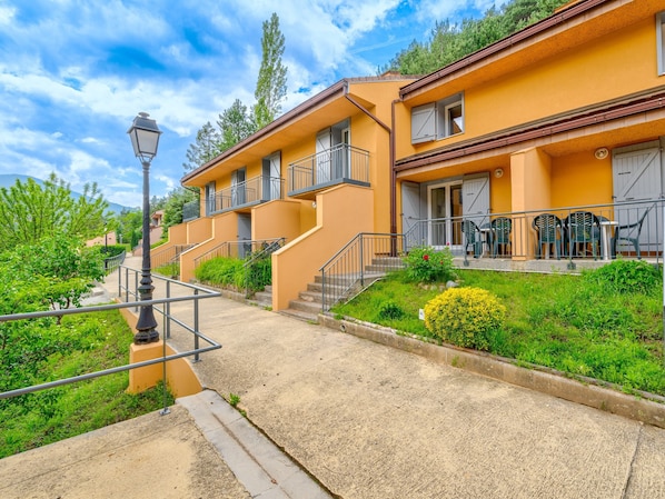 A multi-story building with balconies, a paved pathway, and greenery. - Lovely Apartment for 7-guests (Guillaumes)