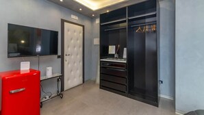 Ett modernt hotellrum med en platt-TV, en röd minibar, en stor garderob och en dörr med en ljuspanel.