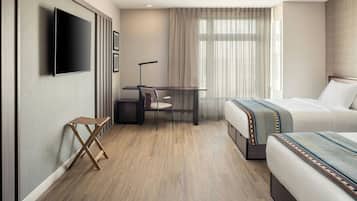 A hotel room with a bed, a desk with a chair, a television mounted on the wall, and a window with curtains.
