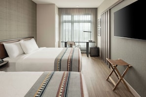 Habitación de hotel con dos camas, un escritorio, una silla, un televisor y una ventana con cortinas.