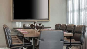 Une salle de conférence équipée d’un grand téléviseur à écran plat, de fauteuils en cuir, d’une table en bois et offrant une vue sur l’extérieur grâce à des rideaux.