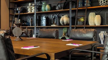 Een vergaderruimte met een houten tafel, lederen stoelen en een boekenkast met diverse decoratieve objecten.