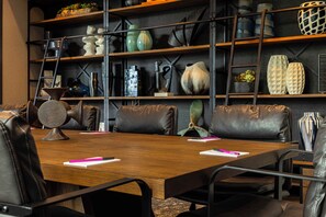 Une salle de conférence avec une table en bois, des fauteuils en cuir et une bibliothèque contenant divers objets décoratifs.