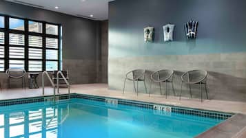 A swimming pool with chairs and a lifeguard chair, a window with blinds, and a wall with towels.