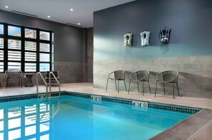 A swimming pool with chairs and a lifeguard chair, a window with blinds, and a wall with towels.