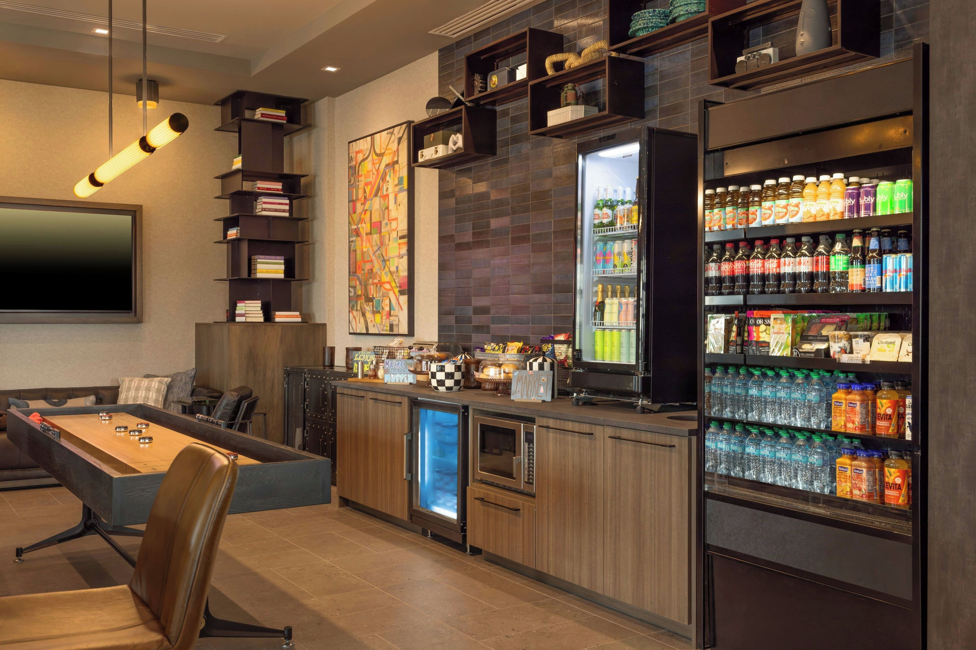 Uma área de bar moderna com mesa de futebol, geladeira abastecida com bebidas e máquina de café.