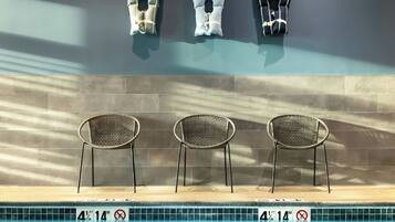 Zona de piscina con tres sillas de mimbre y tres chalecos salvavidas en la pared.