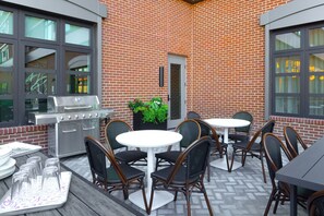 An outdoor patio with a brick wall, a grill, and round tables with chairs. - Moxy Portland Thompson's Point (Portland)