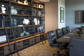 A conference room with a long table, black leather chairs, and a bookshelf with various decorative items. - Moxy Portland Thompson's Point (Portland)