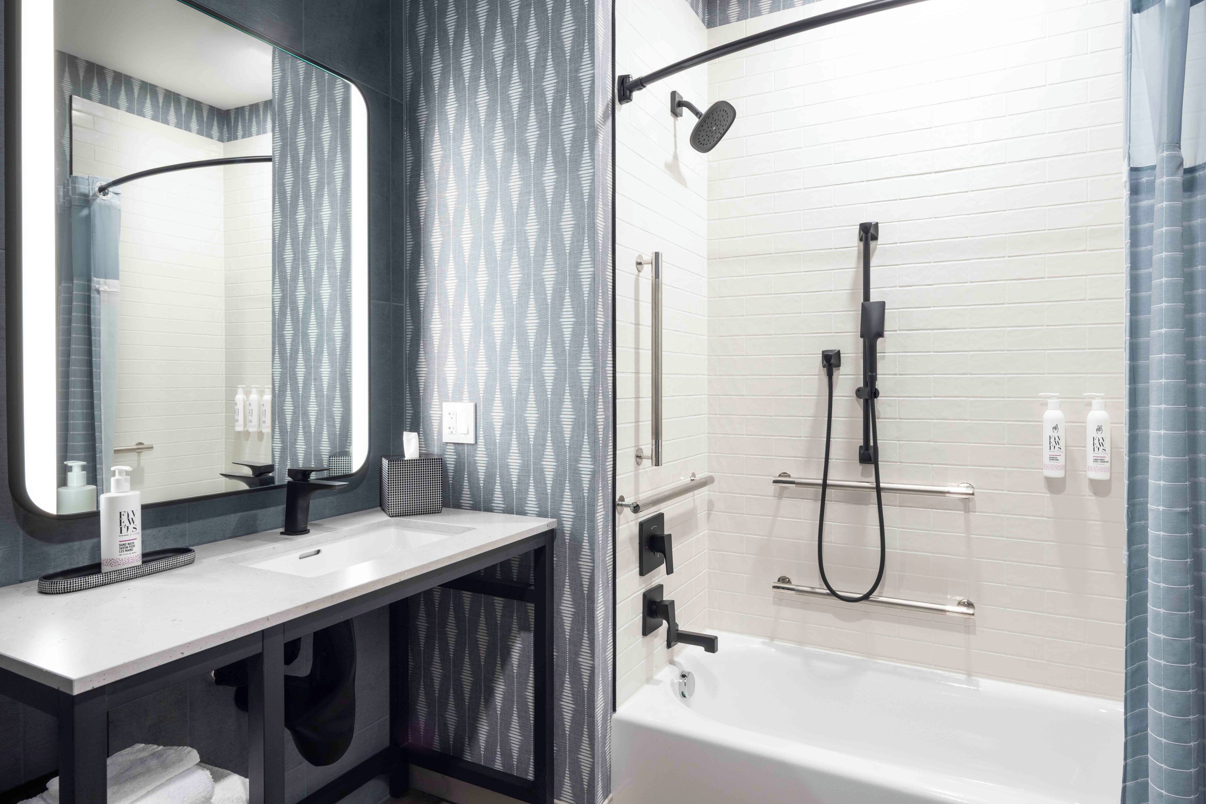 Une salle de bain moderne avec un lavabo blanc, un miroir, une douche équipée d’un pommeau de douche à main et un porte-serviettes.