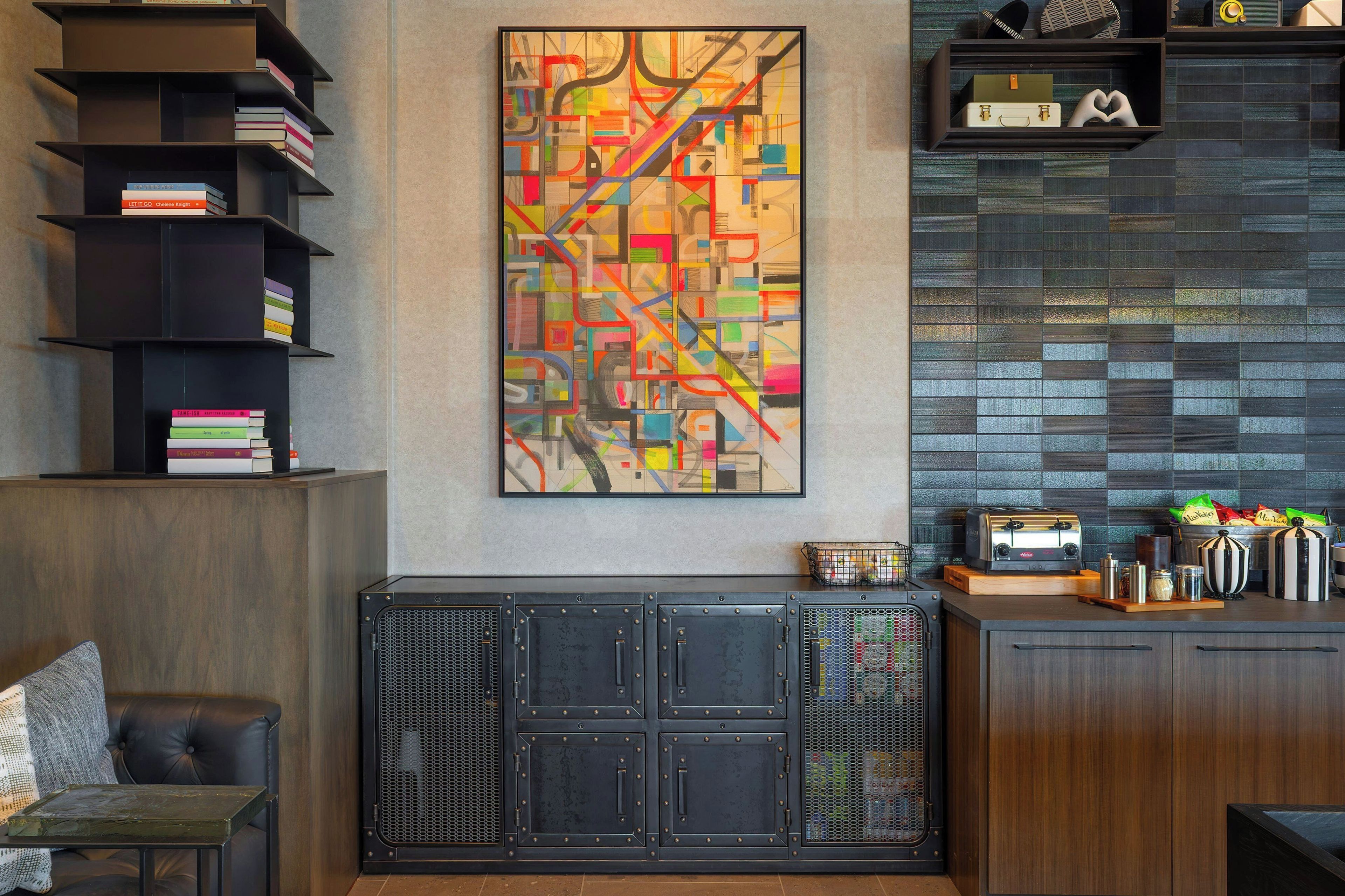 Un intérieur moderne agrémenté d’un grand tableau abstrait, d’une bibliothèque, d’un meuble avec une façade en treillis et d’un coin cuisine  équipé d’un grille-pain.