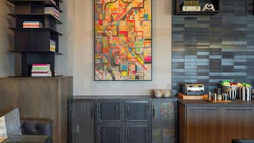 Een modern interieur met een groot abstract schilderij, een boekenplank, een kast met een gaasje voorpaneel, en een keukenhoek met een broodrooster.