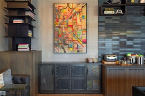 Un interior moderno con un cuadro abstracto grande, una estantería, un mueble con frente de malla y una zona de cocina con un tostador.