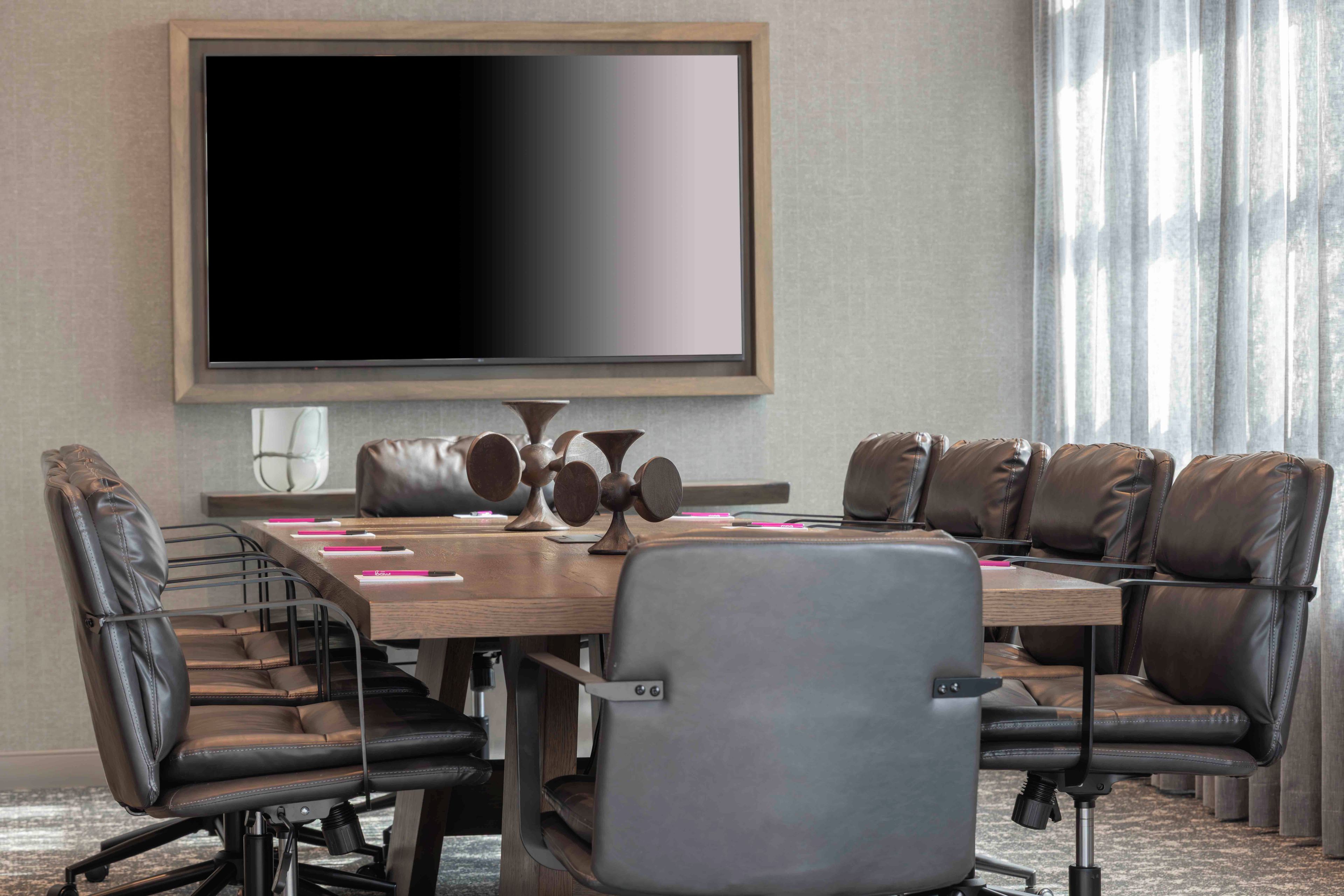 A conference room with a large flat-screen TV, leather chairs, a wooden table, and a projector.