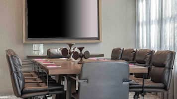 A conference room with a large flat-screen TV, leather chairs, a wooden table, and a projector.