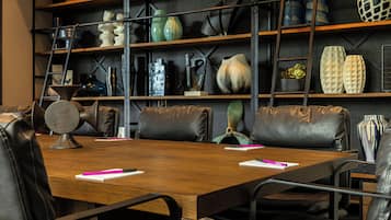 Une salle de conférence avec une table en bois, des fauteuils en cuir et une bibliothèque contenant divers objets décoratifs.