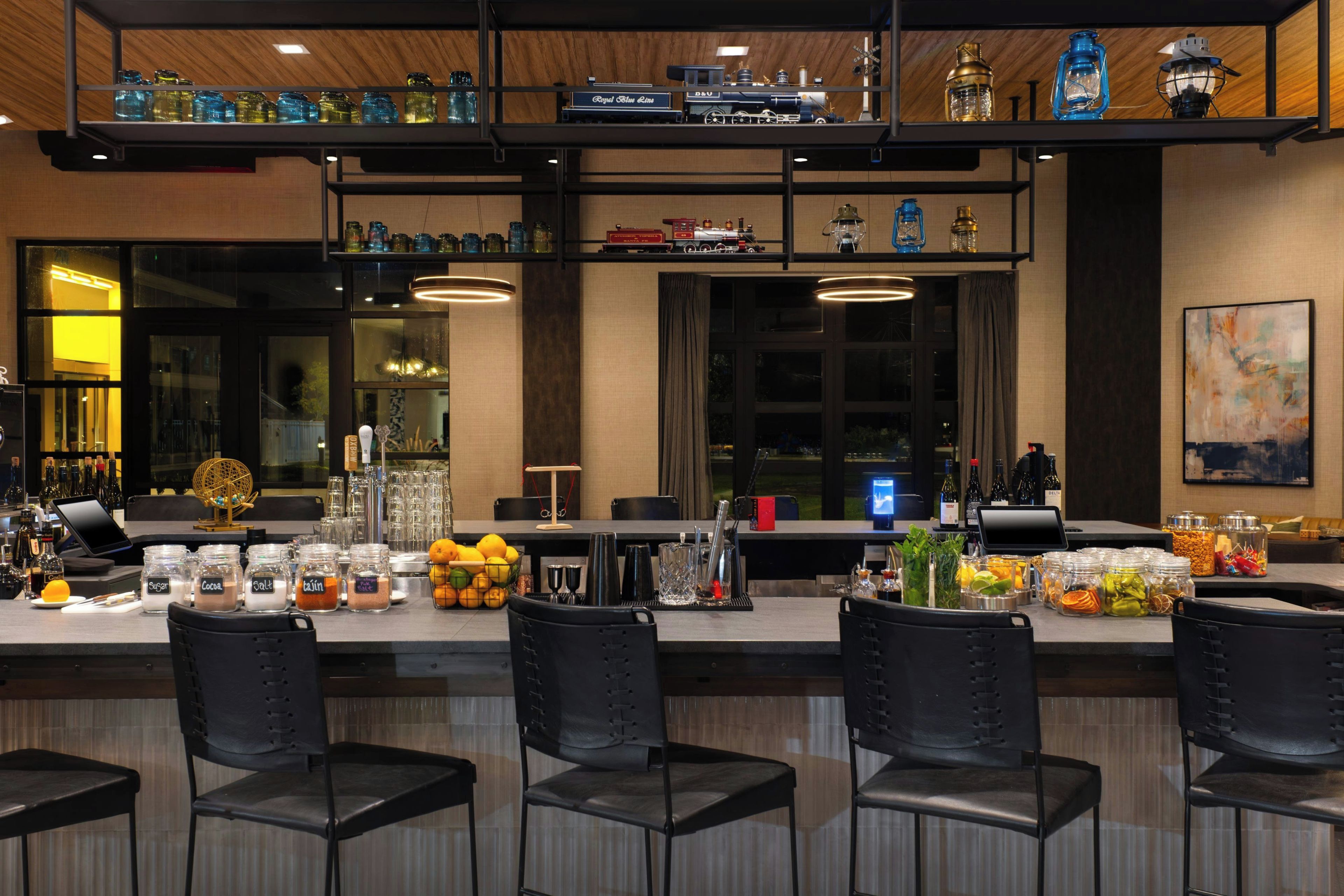 A bar area with multiple seating options, a variety of glassware, and a display of model trains.