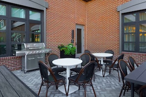 Un patio al aire libre con pared de ladrillo, una parrilla y mobiliario.