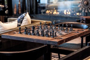 A chessboard with pieces on a wooden table in a room with leather furniture and a fireplace in the background.