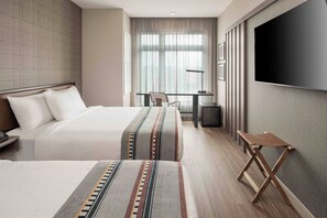 Habitación de hotel con dos camas, un escritorio, una silla y un televisor.