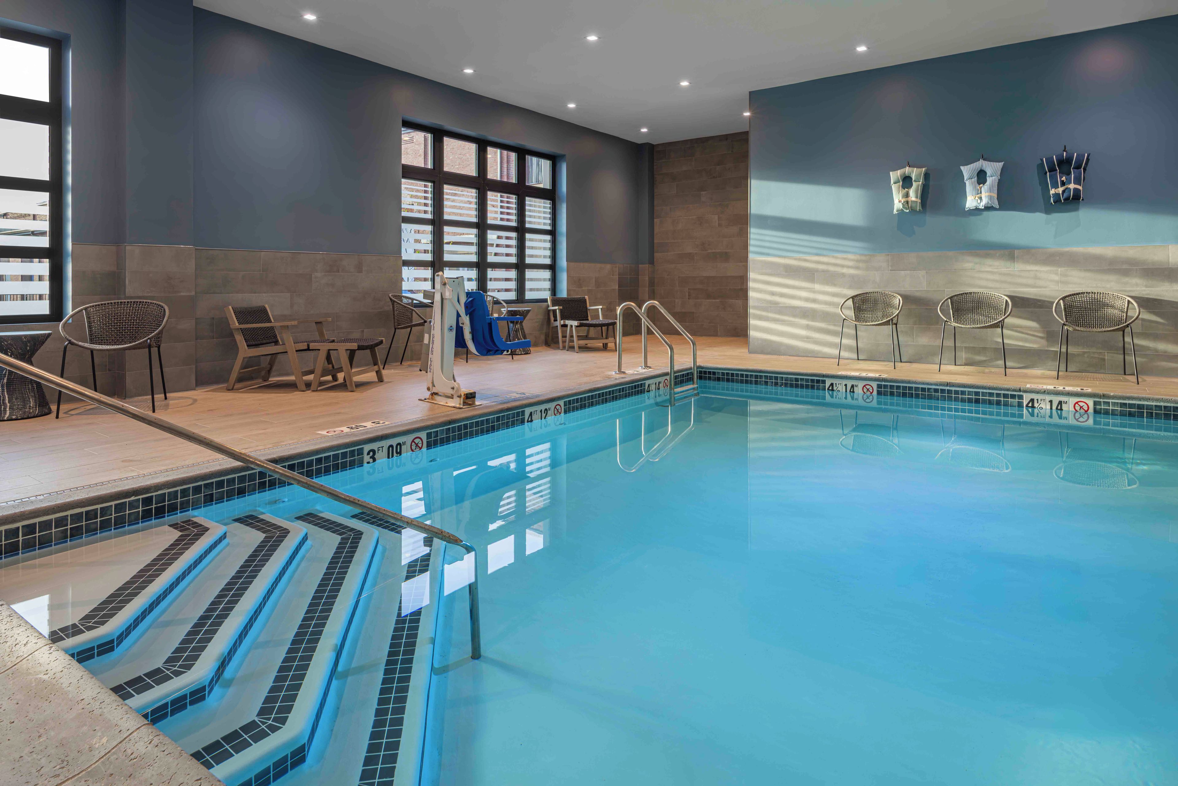 An indoor swimming pool with clear water, a diving board, and lounge chairs.