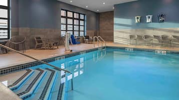 An indoor swimming pool with clear water, a diving board, and lounge chairs.