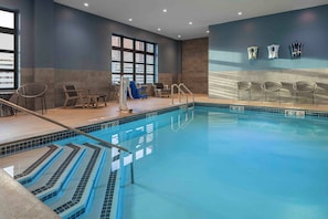 Una piscina interior con agua cristalina, un trampolín y sillas de descanso.