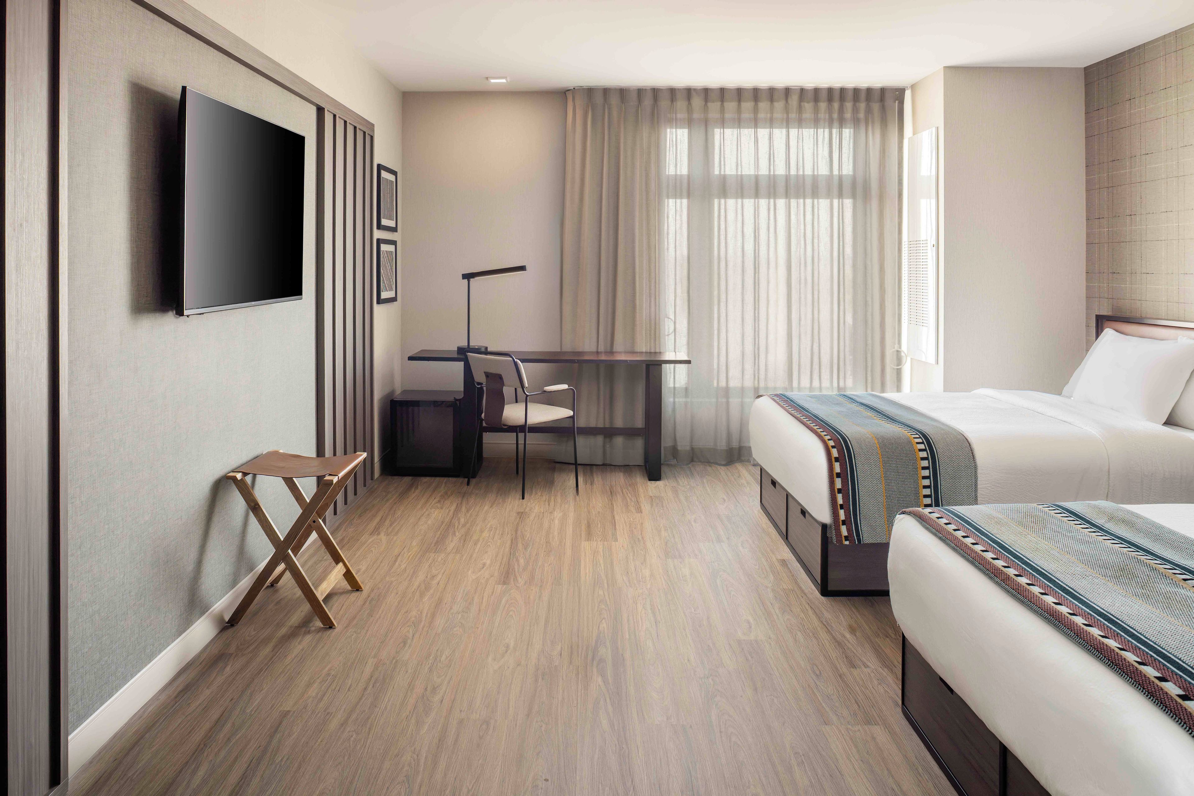 A hotel room with a bed, a desk, a chair, a TV, and a window with curtains.