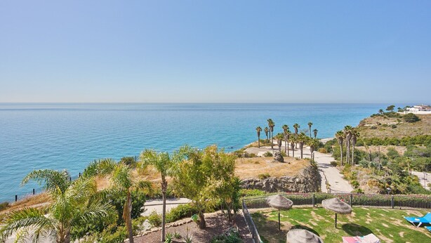 A coastal view with a clear sky, a beach, palm trees, and a pathway leading to a building. - Apartment 'Ocean Vista Calaceite' with Sea View, Swimmingpool and South-facing terrace (Torrox Costa)