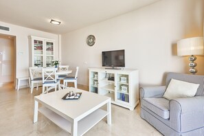 Un salon avec une table blanche, des chaises, un canapé, un téléviseur et un meuble.