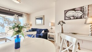 A modern living room with a dining table, chairs, a sofa, a side table, a lamp, and a wall art piece. - Apartment 'Ocean Vista Calaceite' with Sea View, Swimmingpool and South-facing terrace (Torrox Costa)