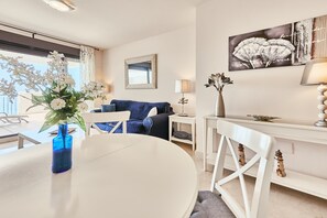 Una sala moderna con una mesa de comedor, sillas, un sofá, una mesita auxiliar, una lámpara y una obra de arte en la pared.