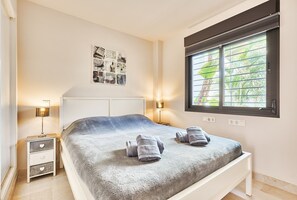 Une chambre à coucher comprenant un lit, deux tables de chevet avec des lampes, une œuvre d’art murale et une fenêtre avec des stores.